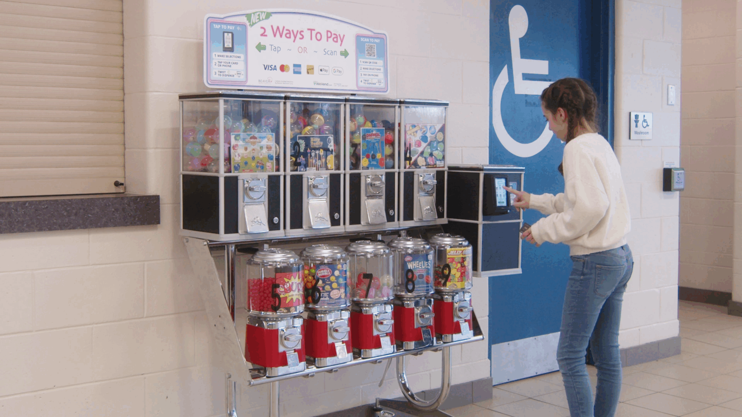 Young woman using a cashless payment terminal on a modern bulk vending machine offering toys and candy in a public location.