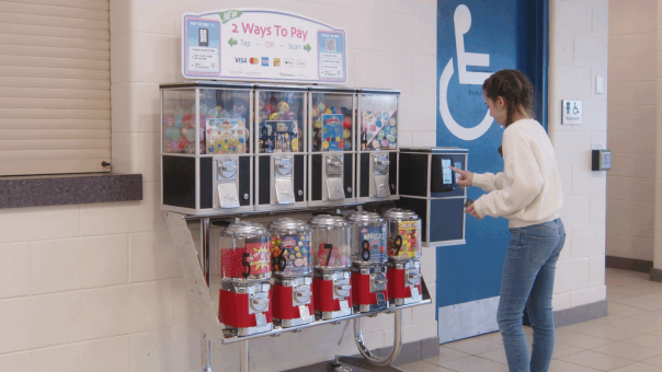 Cashless Bulk Vending Machine Young woman using a cashless payment terminal on a modern bulk vending machine offering toys and candy in a public location.